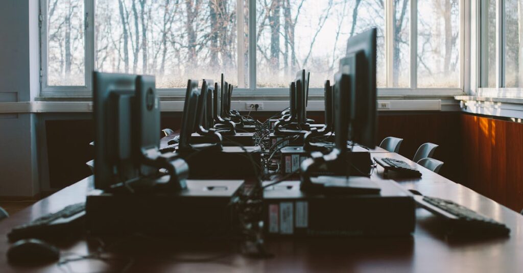 An empty computer lab with multiple workstations and large windows during the daytime.